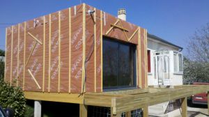 Belle extension ossature bois à SAINT CALAIS (72), avec plancher bois sur pilotis, avec terrasse, bardage red cedar, toit plat, grande baie vitrée avec BSO (Brise Soleil Orientable).